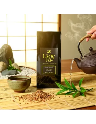Thé vert bio Genmaicha en sachet noir au centre, théière en arrosoir versant eau, tasse et grains de riz autour, feuilles vertes