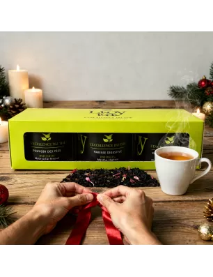 Coffret  L’Excellence du Thé contenant trois boîtes de thé ou infusions, posé au côté d’une tasse fumante et d’un ruban rouge te
