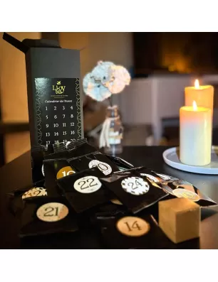 Calendrier de l'Avent noir ouvert avec cases numérotées, certains sachets noirs ; bougies en arrière-plan, ambiance chaude.